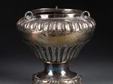 un vase ancien en argent posé sur une table, devant un fond noir