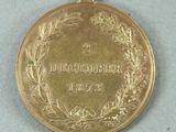 gold medal with a wreath of laurels and the word december on it