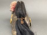 a small doll with long black hair on a gray surface