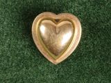 broche dorée en forme de cœur posée sur un tapis vert, sur fond vert
