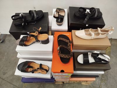 Plusieurs paires de chaussures sont empilées sur des cartons posés sur une table.