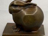 une sculpture en bronze représentant un lapin assis sur une pomme