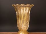 yellow glass vase sitting on top of a wooden table on a black background