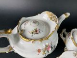two white and gold teapots and a saucer on a black surface