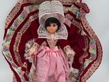 poupée en robe rose et avec un bonnet, assise sur une couverture rouge