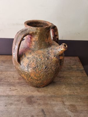 a brown vase sitting on a wooden table with a wall in the background