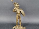 une statue antique en bronze représentant un homme tenant une lance et un bouclier