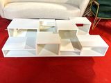 a white coffee table with shelves and a couch in the background
