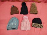 several hats are lined up on a pink blanket on a bed