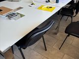 une table blanche avec des chaises noires et un tableau blanc accroché au mur