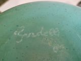 un vase vert orné d'une inscription, posé sur une table