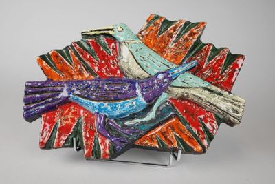 une assiette colorée ornée d'un oiseau, posée sur un socle