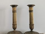 une paire de bougeoirs anciens en laiton posés sur une étagère devant un mur blanc