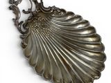 silver plated shell shaped brooch with ornate design on a white background