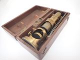 un vieux télescope en laiton dans un coffret en bois, posé sur une surface blanche