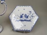 a blue and white plate with a bird on it next to a cup