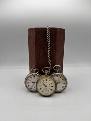 trois montres de poche en argent posées sur un socle en bois