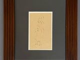 a framed drawing of a woman sitting on a chair in front of a gray wall
