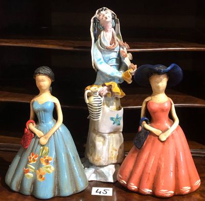 trois figurines représentant des femmes en robe et chapeau, posées sur une étagère