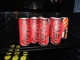 four cans of coca cola sitting on top of a rack in a refrigerator