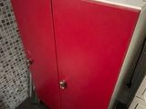 a red cabinet in the corner of a kitchen with a microwave on top of it