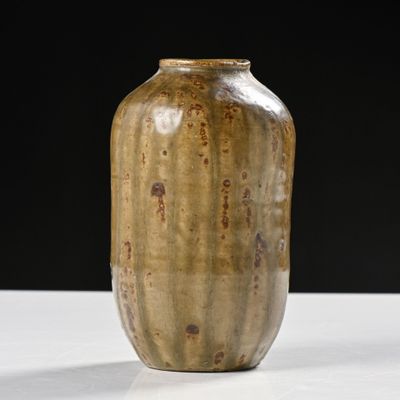 un vase marron posé sur une table blanche, sur fond noir