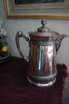 une cafetière en argent posée sur une table, à côté d'une photo encadrée
