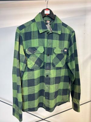 une chemise à carreaux verts et noirs suspendue à un cintre