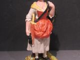 une figurine représentant une femme avec un sac, posée sur un socle
