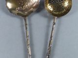 pair of silver spoons with ornate designs on them sitting on a table