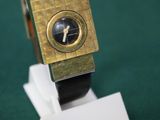 une montre en or posée sur un socle blanc, sur une surface verte