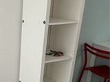 a white cabinet in the corner of a room with a red chair next to it