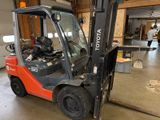 un chariot élévateur garé dans un garage, avec un homme à l'arrière-plan