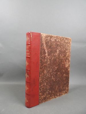 an old book with a red cover sitting on top of a table