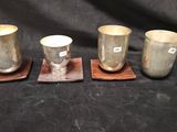 trois tasses en argent et leurs dessous de verre posés sur un tissu noir
