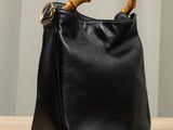 black leather bag with bamboo handle on wooden table in front of curtain