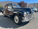 an old black car parked in a parking lot with other cars in the background
