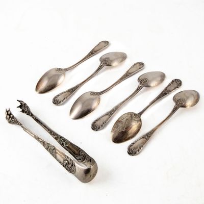 six cuillères et un repose-cuillère alignés sur une surface blanche