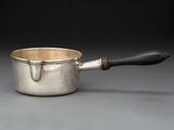 une saucière en argent avec une poignée noire sur un fond gris