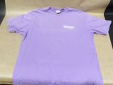 purple t - shirt with white logo on it sitting on top of a chair
