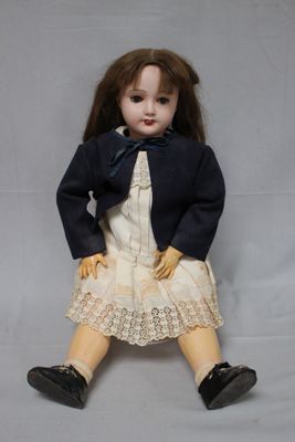 a doll that is sitting on the ground wearing a dress and jacket