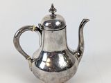 une théière ancienne en argent avec un couvercle, posée sur une surface blanche
