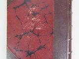 an old book with a red cover sitting on top of a white table