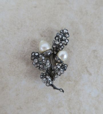 une broche ancienne en argent, ornée de perles et de fleurs, posée sur une surface en marbre
