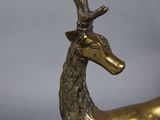 brass statue of a deer laying down on a gray surface
