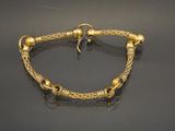 a gold bracelet with a knot and beads on a black surface