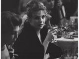 photographie en noir et blanc d'une femme assise à une table avec un verre de vin