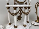 a white marble clock with gold accents on a pedestal