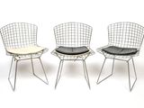 three metal chairs with black cushions on them against a white background