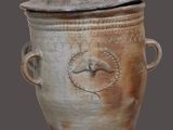 un pot en terre cuite avec un couvercle, sur fond gris